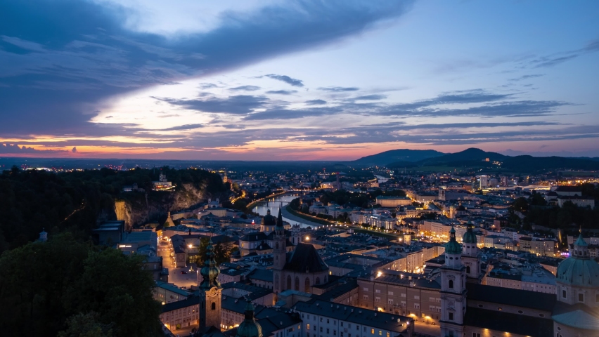 Salzburg city panorama time-lapse at dusk, evening lights, Salzburg historic center with Salzach river and Alps in the background.