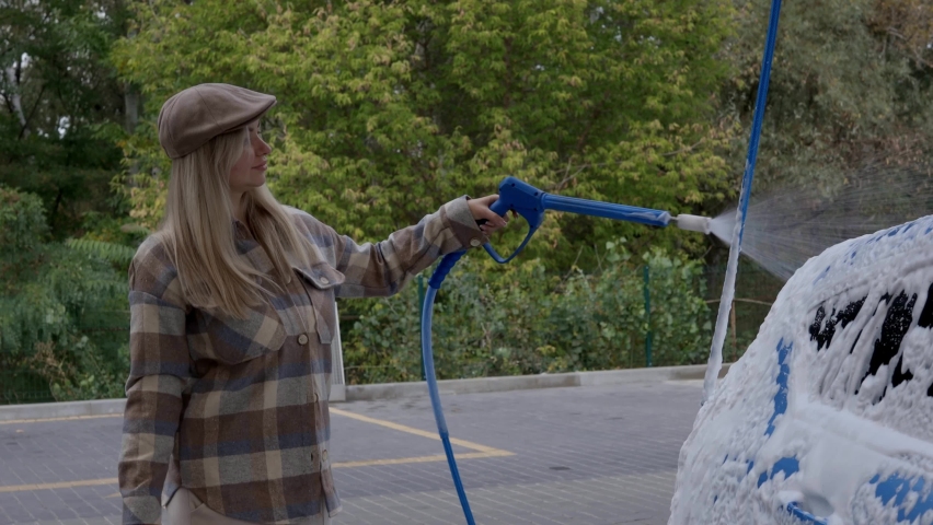 Woman washing a car in a self-service car wash station with wahing foam. Wash car self-service station