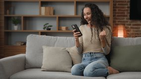 30s Hispanic Latina Caucasian girl woman lady sitting on couch at home living room play with mobile phone win game online betting victory has discount in net virtual hop e-commerce triumph celebrate - Powered by Shutterstock - Get 15% off with code: PIKWIZARD15