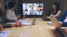 Business people group remote meeting with colleagues via video call conference virtual meeting on tv screen in office at night