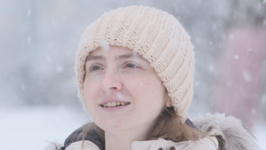 Video portrait of young woman without make up outdoors during snowfall. Girl stares intently at camera. Close up.