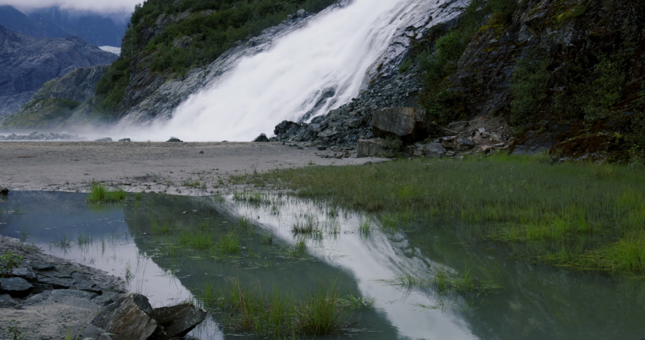 -Beautiful white waters of Nugget Falls, a popular tourist stop north of Juneau, Alaska reflect in small pond at its base making an interesting "V" shaped graphic element