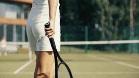 4k video Unrecognizable young woman in white on tennis grass court bouncing the ball before serving. Female playing tennis on sunny day. Tennis club concept.