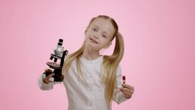 Studio portrait of adorable happy little girl carrying microscope and tube and smiling to camera, enjoying science attributes, pink background, slow motion - Powered by Shutterstock - Get 15% off with code: PIKWIZARD15
