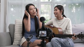 Young Asian lesbian couple blogger vlogger and online influencer recording musical video content playing guitar and singing at home. LGBT lesbian couple performing and  shooting clip for social media.