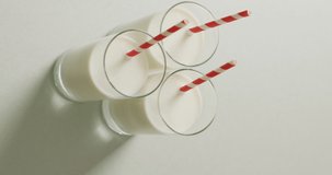 Vertical video of three glasses of milk with red and white straw on grey background. fresh milk and dairy drinks.