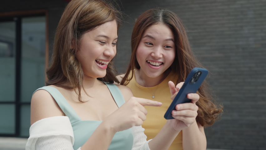 Young Gen Z asia people trending influencer teen girl look at phone enjoy read review and watch viral video laugh joy play social media app post share online fun standing in modern city relax outside. | Shutterstock HD Video #1094826711