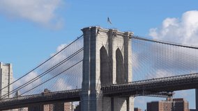 Travel to New York City. 4K video with national flag of America winding on top of iconic Brooklyn Bridge landmark, downtown Manhattan skyscraper office buildings in background.