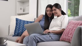 Young Asian lesbian couple video call to their friends and family with laptop.