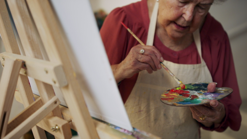 Happy senior woman with artist pallete painting image in atelier.