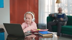 Elementary school pupil in headphones study at home on laptop. Preteen girl in earphones use laptop having online lesson sitting at table in living room