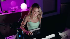 Young blonde woman streamer playing video game using computer at gaming room