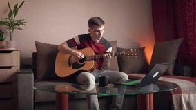 Young man learning to play acoustic guitar online at home