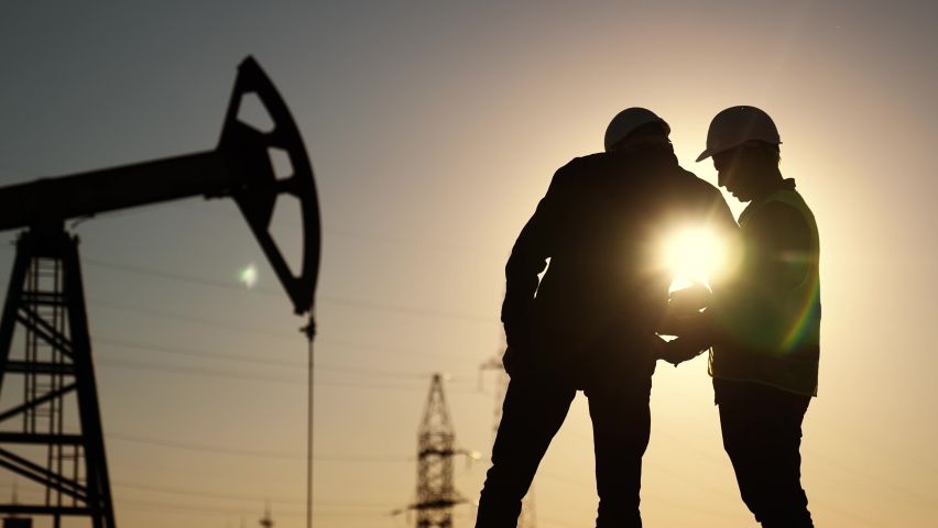 oil production. two silhouette workers work as a team next to an oil pump. business oil production production concept. two engineers of sun the oil and gas industry are discussing a business plan Royalty-Free Stock Footage #1094839545