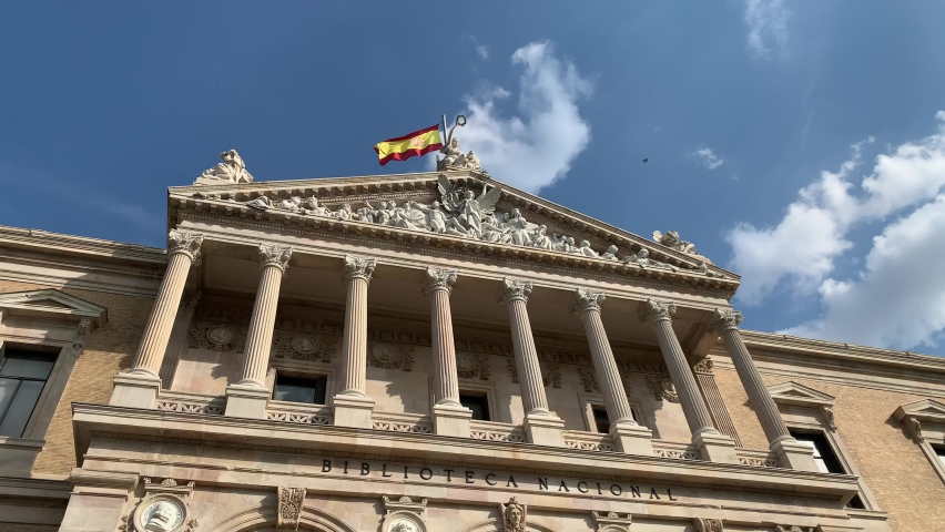 Spanish flag is waving on top of National Library of Spain (Biblioteca Nacional de Espana). Main, front entrance, facade. It is one of the largest libraries in the world. Madrid, Spain 