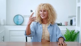 Attractive young Caucasian woman blogger holding smartphone in her outstretched hand and looking at the web camera, recording a video content for her blog or having online conversation. Selfie mode