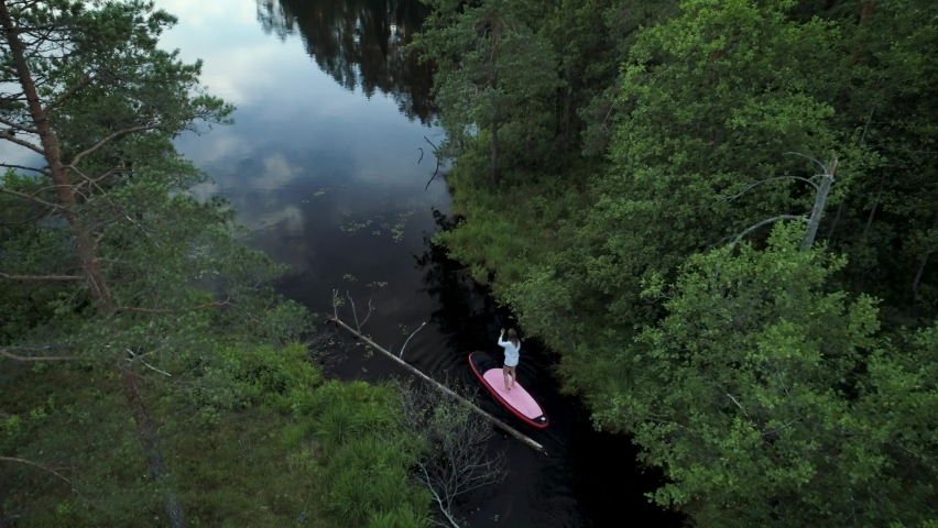Woman is exploring tight lake path on SUP board.