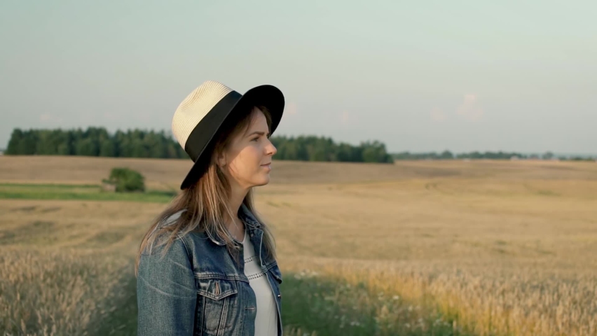 Girl is saying hello to someone by waving her hand up in the air. Woman is dressed with denim jacket and summer style hat. She looks like happy traveler on her holidays traveling around the country. Royalty-Free Stock Footage #1094850995