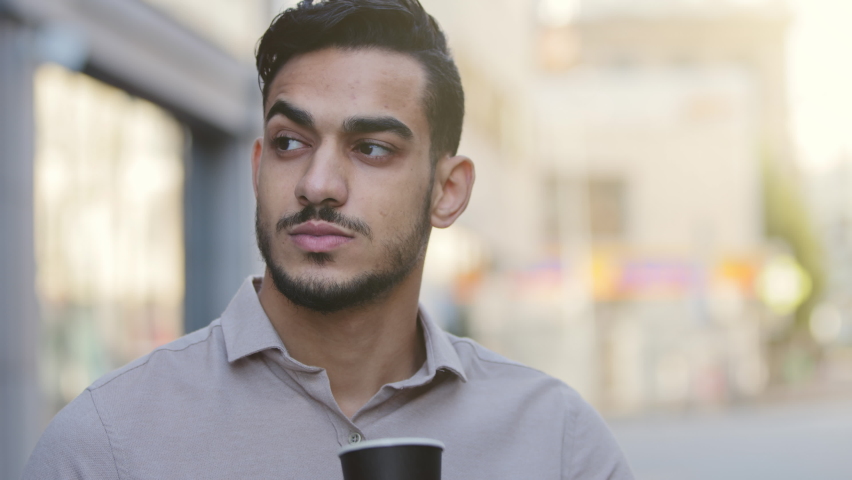 Close up portrait 30s bearded Hispanic Indian man standing in city street looking around thoughtful pensive drinking tea from paper cup. Businessman thinking resting outdoors drinks coffee has break | Shutterstock HD Video #1094852247