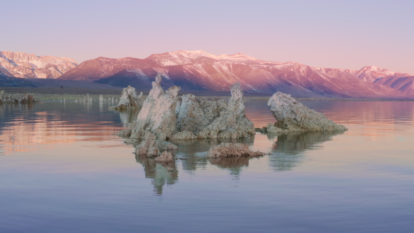 Amazing pink lake with calm surface and sunrise sky reflection. Cinematic aerial drone view colorful pink lake with tufa formations coast landscape. Amazing Mono lake in Sierra Nevada Mountains USA 4K