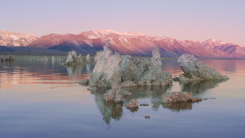 Amazing pink lake with calm surface and sunrise sky reflection. Cinematic aerial drone view colorful pink lake with tufa formations coast landscape. Amazing Mono lake in Sierra Nevada Mountains USA 4K