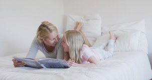 Animation of butterflies over happy caucasian mother and daughter reading book in bed. family life, childhood, love and care concept digitally generated video.