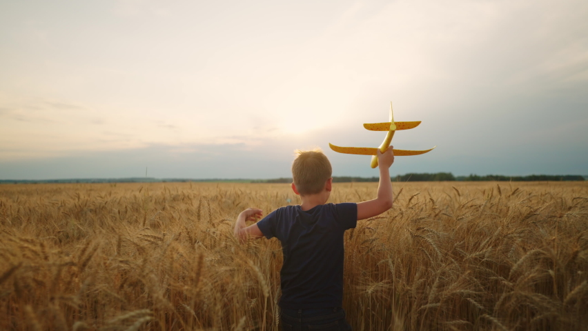 Charming little boy with toy plane in hand is running on golden rye field, rear view against cloudy sky | Shutterstock HD Video #1094854137