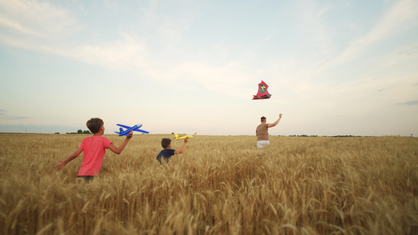 Little boys are running together in gold wheat field in summer, flying kite and toy planes | Shutterstock HD Video #1094854321