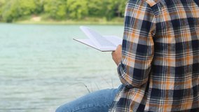 Man reading book by the lake, peaceful and relaxing activity in nature, reading a book concept, man with shirt sitting and read storybook, 4k 60 fps video, one person, leisure and enjoyment idea