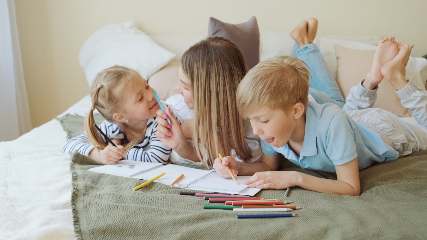 Family leisure, mom and kids lay on bed and draw pictures on paper in their apartment room. Educational games, happy friendly family, parents and children relationships | Shutterstock HD Video #1094856949