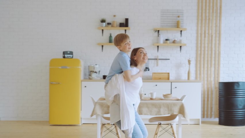 Loving happy mother carries her little son on her back, having fun at home, in living room. Active parents and children concept, family relationships | Shutterstock HD Video #1094856951