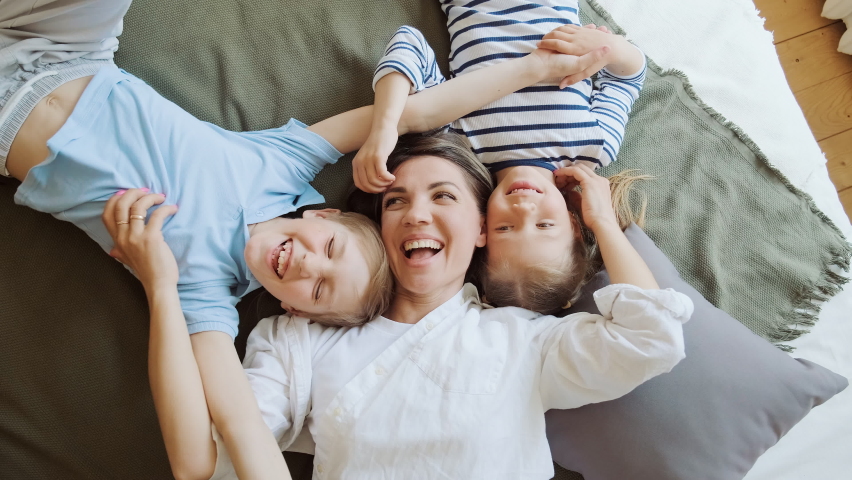 Happy mother with two children laying on bed at home having fun and playing. Son and daughter with their mom babysitter laugh and smile, tickle each other, true emotions | Shutterstock HD Video #1094856953