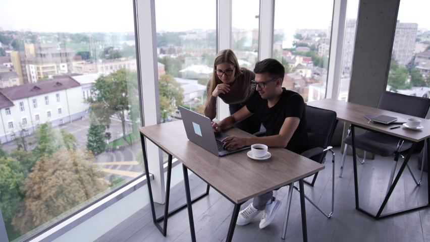 Colleagues look at the laptop screen point at it and discuss. Cooperative teammates solving work issues and brainstorming. Cityscape in window. | Shutterstock HD Video #1094857915