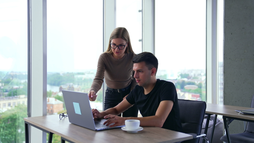 Office teammates cooperating and discussing work. Male and female colleagues looking at laptop talking and smiling. Blurred backdrop. | Shutterstock HD Video #1094857917