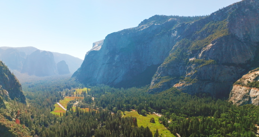 Flying over the picturesque green valley covered with pine tree woods. Sunny scenery of rocks in Yosemite National Park, USA. Top view.