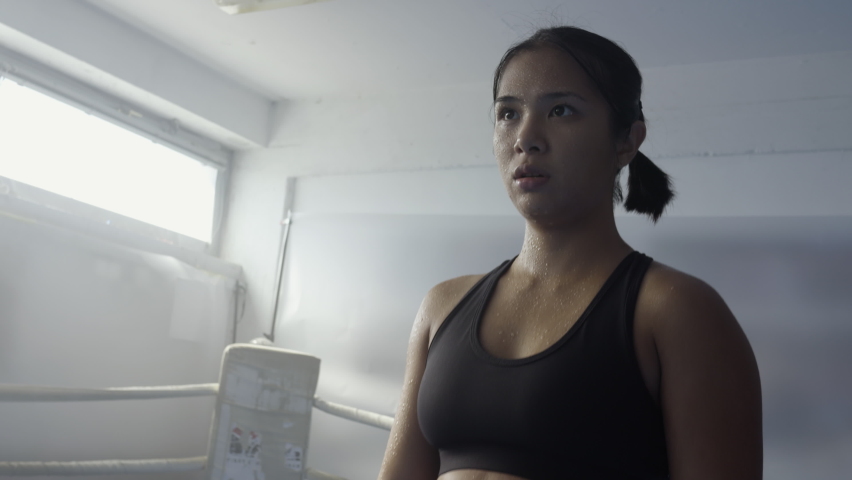 Young female kickboxer raising up hands in gloves, showing winner gesture. Kickboxing workout, strong girl training in gym, handheld shot