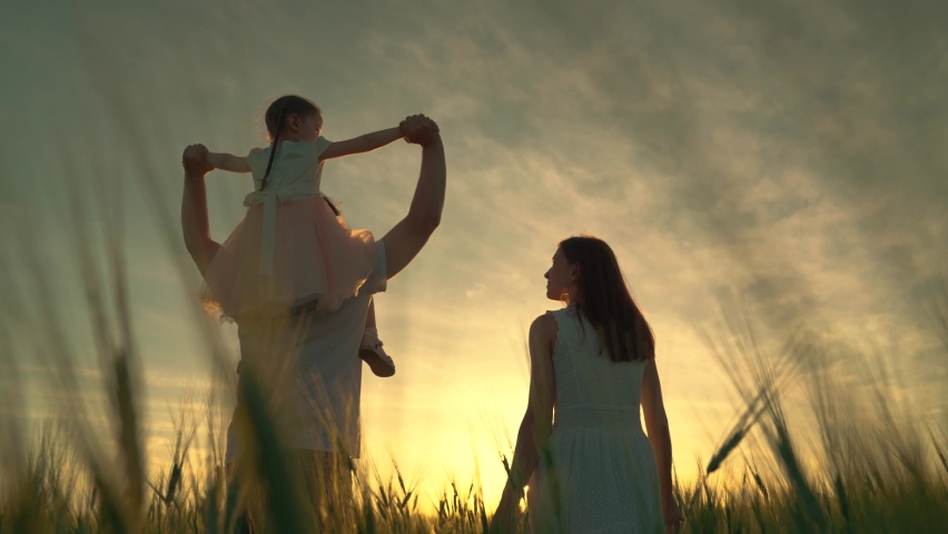 Young mother, father and little daughter play, enjoy nature outdoors, kid's dream of flying. Mom, dad and child walk together, family of farmers with child on their shoulders walks through wheat field Royalty-Free Stock Footage #1094868989
