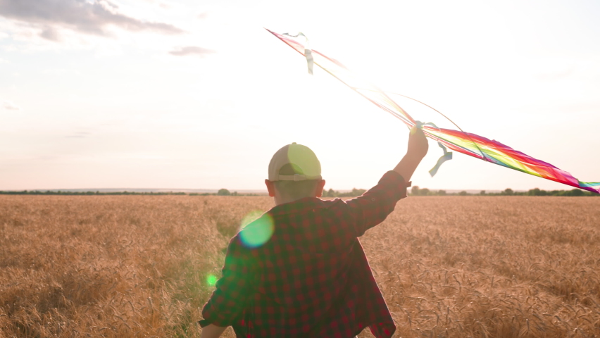 Kite hovers flies in hand of kid. Boy with toy kite, Son plays at sunset, dreams of flying, traveling. Active Child runs with kite in sun. Happy boy runs in field of wheat, plays with toy kite. | Shutterstock HD Video #1094869657