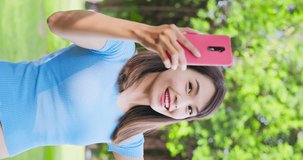 vertical of asian young woman has video chat with friends happily through smart phone in the park or campus