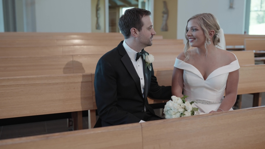Bride and groom kissing while sitting on a wooden pew in a modern church. Dolly shot. | Shutterstock HD Video #1094873609