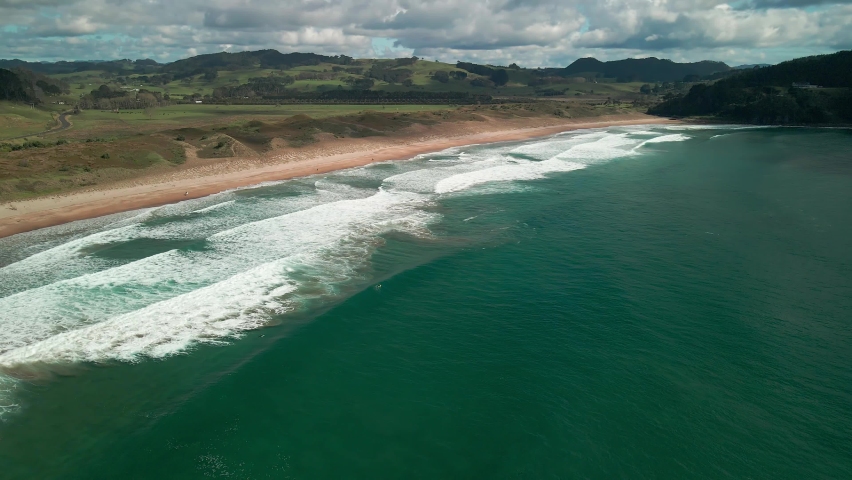 Cinematic drone flight over surf break with mountains in the background