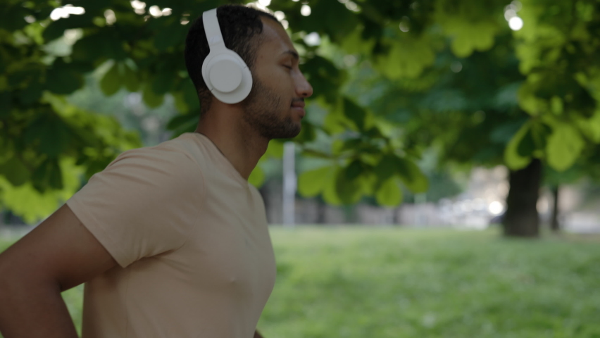 Side view of the african american man running in the park wearing headphone in the middle of the day. Sport and healthy lifestyle concept | Shutterstock HD Video #1094876147