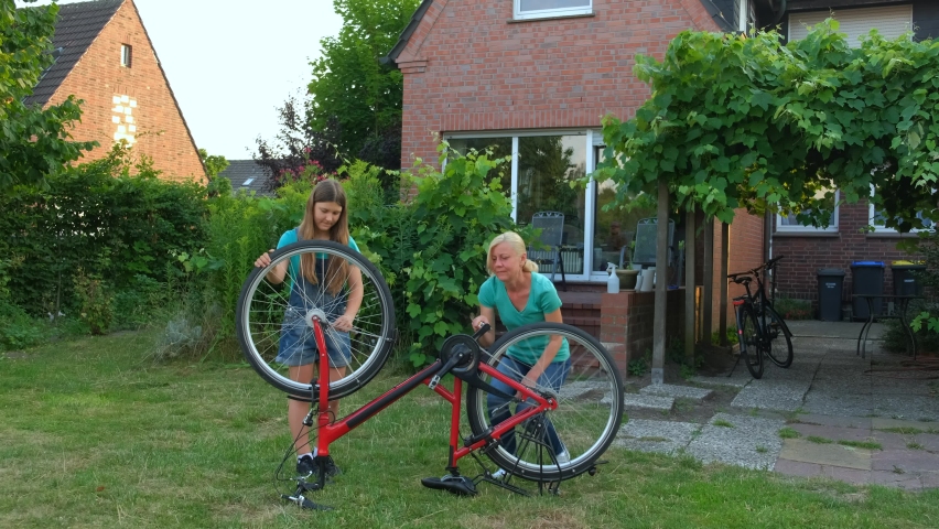 Mom helps her daughter fix her bicycle in the backyard of the house. Happy, friendly, considerate mother. | Shutterstock HD Video #1094877245