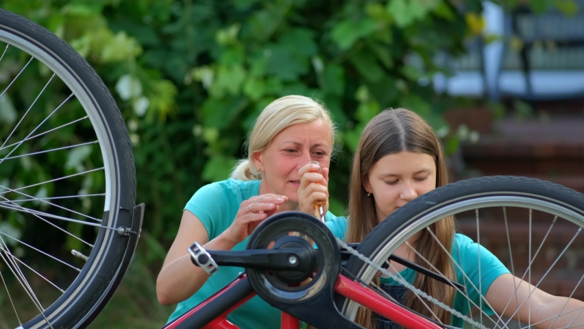 Mom teaches her daughter how to fix her bicycle in the backyard. Happy, friendly, considerate mother. | Shutterstock HD Video #1094877249