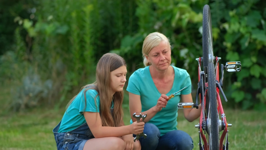 Mom teaches her daughter how to fix her bicycle in the backyard. Happy, friendly, considerate mother. | Shutterstock HD Video #1094877251