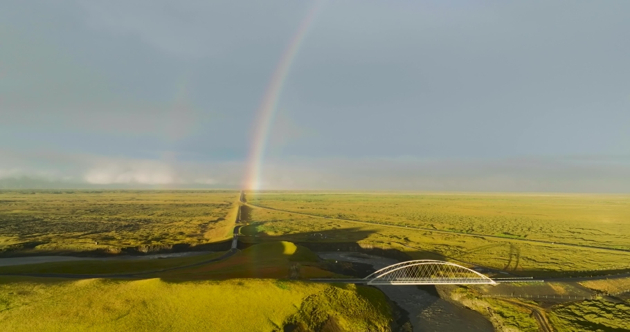 Aerial view of double rainbow over green landscape with roads and bridge with low standing sun, south Iceland.