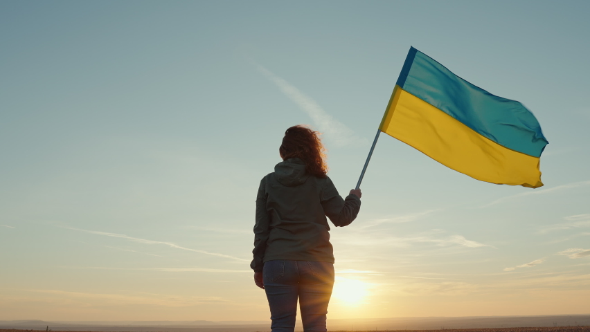 Flag Ukraine Young woman stands in her hand waving in wind background of golden sunset, disk of sun in field of peaceful sky. No war. Freedom. Patriotism. Refugees | Shutterstock HD Video #1094883947