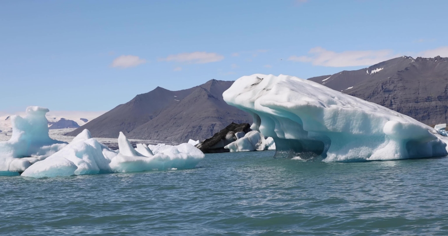 Icebergs melt in the sun in a vast blue Jokulsarlon glacier lagoon in the interior of Iceland under climate change and global warming | Shutterstock HD Video #1094883991