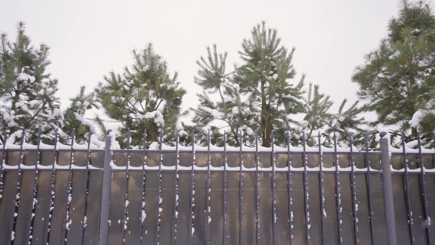 Snow flakes slowly fly against the background of the fence of the house. Snowfall in winter in the village. Cozy mood, calmness. Snowfall in the village against the background of a fence and Christmas