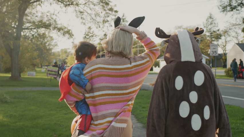 Woman with two children in carnival costumes in honor of Halloween. Walking down the street of a small American town